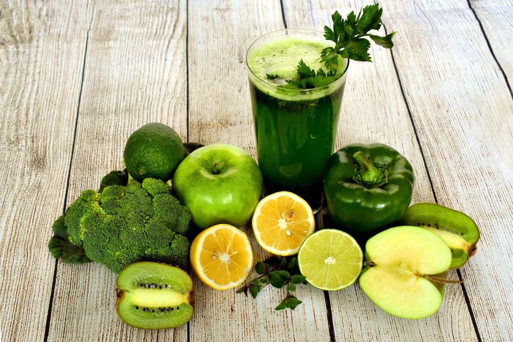 Green smoothie surrounded by fresh fruit and vegetables on a wooden table