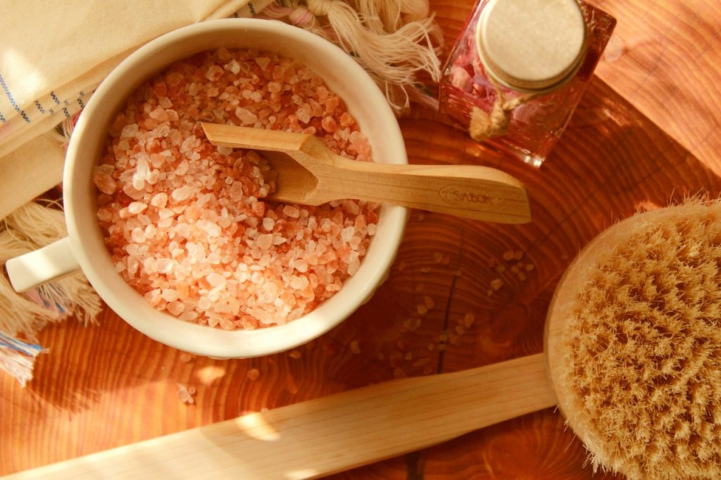 Bowl of pink bath salts with a wooden scoop and bath brush