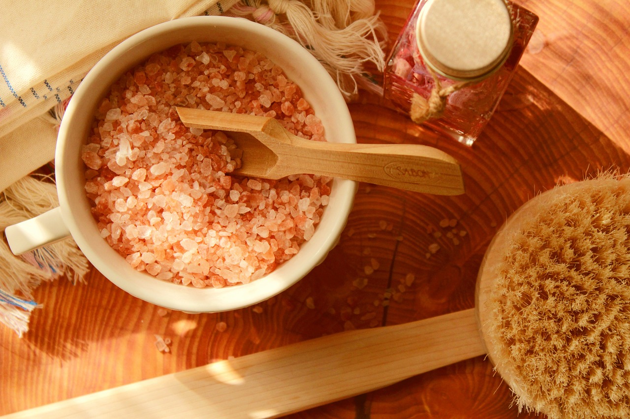 Bowl of pink bath salts with a wooden scoop and bath brush