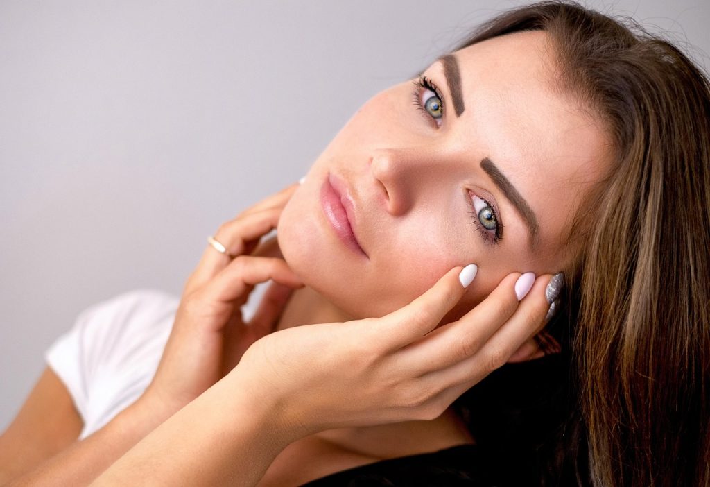 Woman gently touching her face in soft light, skincare concept