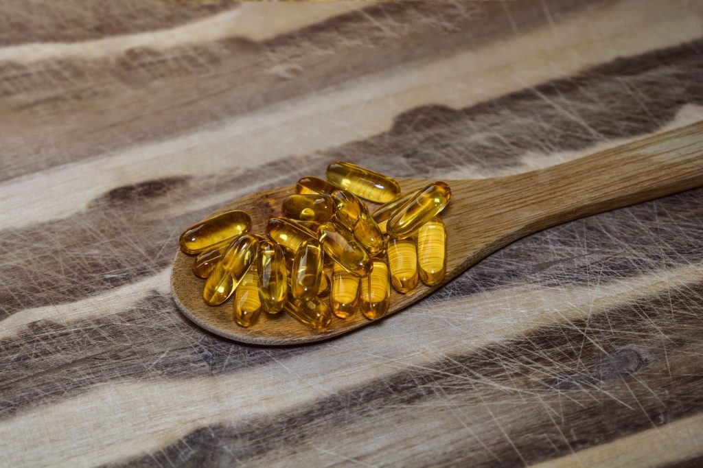 Golden softgel supplements on a wooden spoon
