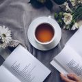 Laure, writer and editor at Essence Vale, reading with a cup of tea and fresh daisies